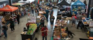 A large indoor market with several booths selling a variety of pet supplies. There are people shopping at the booths and dogs walking around.